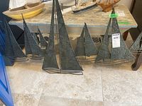 Photo showing the entire metal sailboat wall art piece with several sailboats arranged side by side on the floor beneath a wooden table.