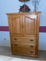 Front view of wooden armoire showing two doors on top and three drawers below with ornate brass handles.