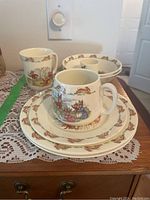 Full set of Bunnykins children's dishware arranged to show plates, bowls, cups, and egg cup with distinctive Bunnykins rabbit character designs and borders.