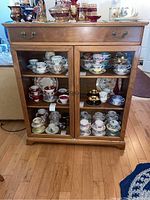 Front view of wood cabinet with glass doors showing shelves inside with various dishware items on display.
