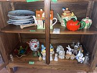 Wide view of two shelves showing a collection of ceramic teapots, salt and pepper shakers, blue and white plates, and collector plates.