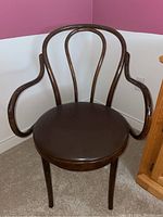 Front view of the wooden chair showing the curved armrests and round vinyl seat in dark brown color.