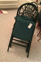 Four folded metal framed chairs with dark green fabric seats stacked together.