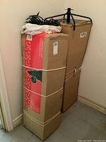 Two boxes containing the Christmas trees and metal stand tied with string against a wall.