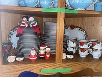 Full view of the Christmas dinnerware set including stacked plates, cups, saucers, salt and pepper shakers, and candle holders, all displayed in a wooden cabinet.