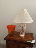 Full view of the painted glass base table lamp with fabric shade alongside the art glass vase on a wooden surface.