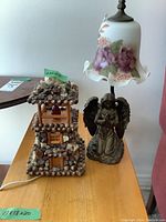 Photo of the table lamp made of stones and shells shaped like a lighthouse and resin angel lamp with glass shade on a surface.