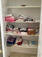 Linen closet shelves filled with neatly folded linens in various colors and styles including doilies, tablecloths, tea towels, and sheets.