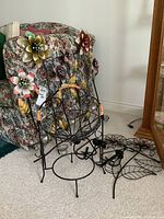 Photo showing black metal fruit basket in front, metal wall flowers attached to furniture behind, and black metal wall candle holder to the right on carpet.