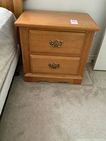 Photo of first solid wood nightstand with two drawers and metal handles, showing wood grain finish and top surface.