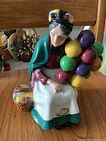 Front angled view showing the figurine's detailed facial features, bonnet with floral pattern, and colorful balloons.