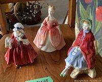 Three Royal Doulton figurines displayed on wooden surface showing all three distinct pieces.