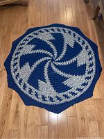 Full view of the round braided rope rug with blue and beige pinwheel pattern laid on a wooden floor.