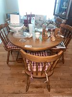 Full view of the wood dining table with six attached chairs around it, showing checkered cushions and various tabletop items.