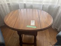 Front view of oval wooden table with central section and side drop leaves folded down
