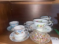 Full set of five teacups and saucers showing various floral designs and gold accents