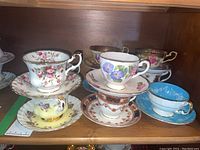 Shelf display showing six teacup and saucer sets in varied colors and patterns