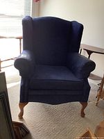 Front view of the blue velour wingback chair showing plush cushioning and cabriole wooden legs.