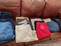 15 pairs of men's pants arranged on sofa showcasing variety of colors and styles including denim, casual, and khaki pants.