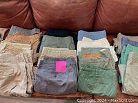 20 men's shorts neatly folded in stacks on couch, mixed colors including beige, gray, green, blue, tan
