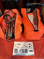 Two orange beach sunshades in zippered bags filled with metal poles, cords, and fabric.