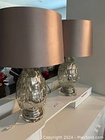 Pair of matching lamps featuring silvered textured glass bases with copper-colored drum shades, shown on a white surface.