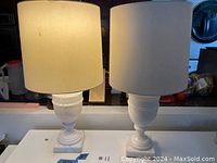 Two white alabaster or alabaster-like table lamps with fabric drum shades displayed on a counter.