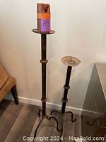 Pair of two tall iron candleholders standing side by side with one holding a purple candle.