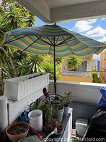 Photo showing umbrella open on patio with surrounding plants and multicolored striped fabric canopy.
