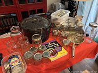Wide view of all items on table showing pot, many mason jars, utensils in plastic container, and canning book
