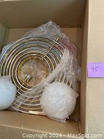 Parts of chandelier in original box showing nested gold-tone spiral rings and bubble-wrapped glass globes