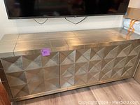 Front view of gold-tone hammered metal credenza with four doors and geometric pattern.