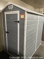 Front view of assembled garden shed, showing grey resin panels, white trim, closed single door with black hardware