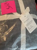 Photo of the curtain folded and wrapped with a white fabric tie, showing the Pottery Barn tag indicating it is a 3-in-1 pole top curtain in Seaton Textured fabric.