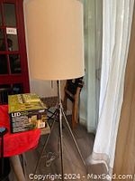 Tripod floor lamp with white fabric drum shade and polished metal base.