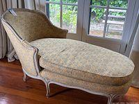 Side view of antique French settee chaise lounge showing curved arm, patterned upholstery, and wooden carved frame.