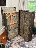 Full view of the antique steamer trunk open with interior compartments and lining visible.