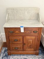 Full view of antique Victorian wash stand showing wood base with drawers and door, and white marble top with backsplash and side wings.