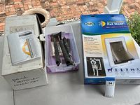 Photo showing large white box labeled 'paint remover machine,' a plastic container holding black-handled paint scrapers, and a blue PetSafe Extreme Weather Pet Door box.