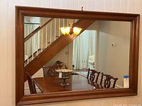Front view of large rectangular wall mirror showing solid wood frame and reflection of dining room furniture and chandelier.