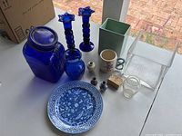Overview of all items in the lot arranged on white surface including cobalt glassware, ceramics, vintage mug, and plate.