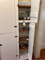 Full view of six white shelves inside a cupboard featuring assorted kitchenware including glass bowls, metal bowl, and papers at bottom shelf.