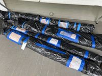 Ten rolls of upholstery fabric wrapped in black bags, arranged on floor for sale.