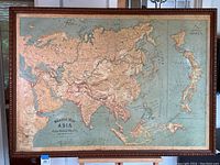 Full view of the framed relief map showing the entirety of Asia with visible relief of mountain ranges and terrain, framed with carved wood.