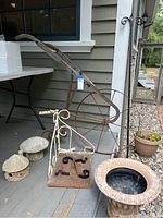 Antique hand plow with rusty iron wheel and wooden handles alongside decorative items including mushroom and gnome house ceramic pieces, corner shelf, and composite plant pot visible on porch.
