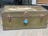 Front view of vintage military foot locker with three latches and taped center lock