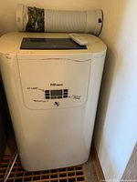 Front view of Danby Premiere air conditioner unit with vent duct attached and remote on top. Panel shows channel layout and button labels.