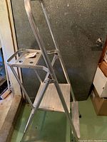 Angle view of the aluminum ladder showing two steps and the top shelf with holes, highlighting its construction and folding capability.