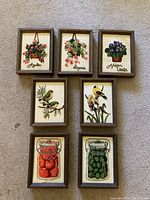 Seven framed needleworks arranged on carpet showing all items and details