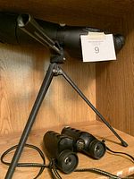Bushmaster spotting scope with tripod visible on wooden floor, showing adjustable eyepiece and tripod legs open.